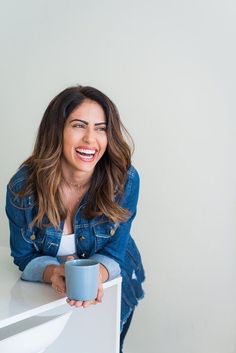 a woman sitting at a table with a cup in her hand and smiling for the camera