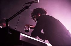 a man sitting at a keyboard with a glass of wine in his hand and a microphone behind him