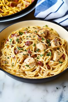 pasta with chicken and bacon in a pan on a marble countertop next to another dish