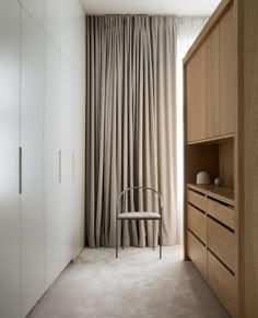 a chair sitting in front of a window next to a cabinet and cupboard with curtains on it