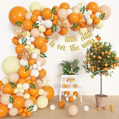 an orange themed birthday party with balloons and greenery on the wall, potted tree