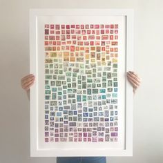 a person holding up a framed art print with stamps on it's sides and hands