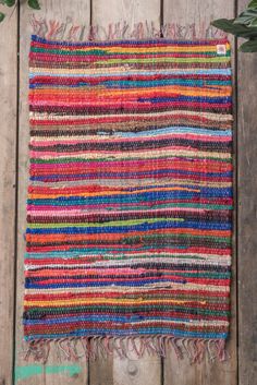 a multicolored rug with fringes on top of a wooden floor next to a potted plant