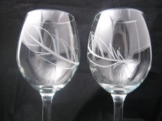 two clear wine glasses sitting next to each other on a table with a black background