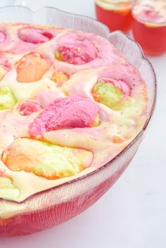 a cake with pink and yellow icing on it sitting in a glass dish next to other desserts