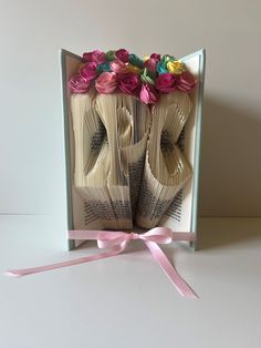 an open book with folded pages and flowers on top, tied to a pink ribbon