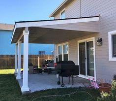 a patio covered with an awning and grilling area next to a house on a sunny day