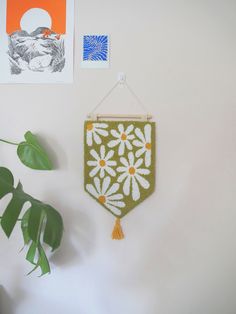 a green wall hanging with white daisies on it and two pictures above the hanger