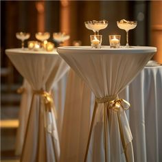 two tables with candles on them and white tablecloths draped around the top one