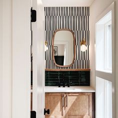 a bathroom with black and white striped wallpaper on the walls, wooden cabinets and a round mirror