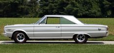 an old car parked on the side of the road in front of some grass and trees