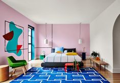 a bedroom with pink walls, blue rugs and colorful artwork on the wall above the bed