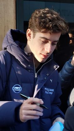 a man in a blue jacket is looking at his cell phone and writing on it