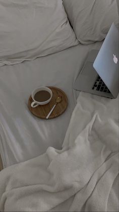 an apple laptop computer sitting on top of a bed next to a wooden tray with a cup of coffee