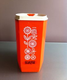 an orange trash can with white flowers on it and the word sugar written in red