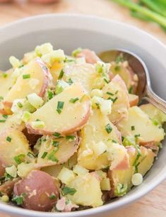 a bowl filled with potato salad on top of a wooden table next to green onions