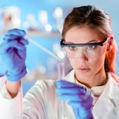 a woman in lab coat and goggles holding up a test tube with blue liquid