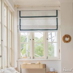 a bedroom with white walls and windows has an ottoman in front of the window, along with a wicker basket on the floor