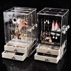 two clear jewelry boxes with earrings and earring holders in them on a black surface