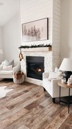 a living room with white couches and fireplace in the center, surrounded by wood flooring