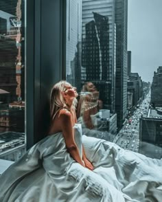 a woman sitting on top of a window sill looking out at a cityscape