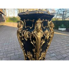 an ornate black and gold vase sitting on top of a brick sidewalk in front of a house