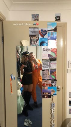 two women standing in front of a mirror with posters on the wall behind them and one woman taking a selfie