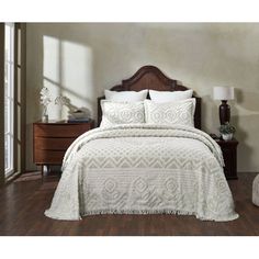 a bed with white bedspread and pillows in a room next to a dresser