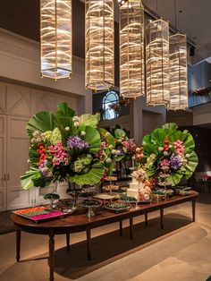 a table topped with lots of flowers and greenery next to a chandelier