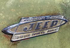 an old jeep emblem on the side of a green vehicle with rusted metal lettering