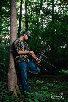 a man holding an arrow while leaning against a tree in the middle of a forest