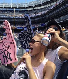 two women are holding up signs at a baseball game while one woman is brushing her teeth