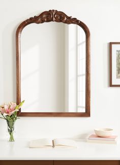 a mirror sitting on top of a table next to a vase with flowers