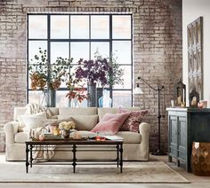 a living room with brick walls and furniture in front of a large window that has potted plants on it