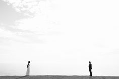 two people standing on top of a sandy beach