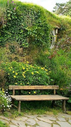 a wooden bench sitting in front of a lush green wall covered with plants and flowers