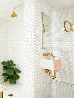 a white bathroom with gold fixtures and a pink plant in the corner next to the sink