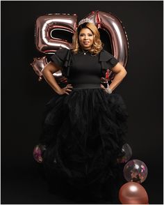 a woman in a black dress standing next to balloons and heliums with the number twenty two on it