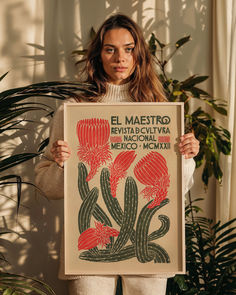 a woman holding up a poster in front of a plant with red flowers on it