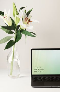 a laptop computer sitting next to a vase with flowers in it