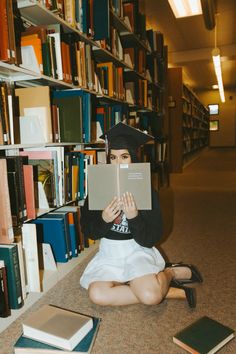 a woman sitting on the floor in front of bookshelves holding up a book