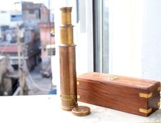 a wooden box sitting on top of a window sill next to an old fashioned telescope