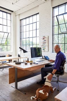 a man sitting at a desk with a dog laying on the floor in front of him