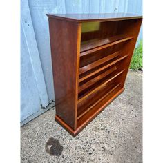 a wooden cabinet sitting on top of a cement floor next to a wall and grass