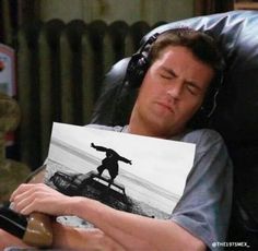 a man laying in a chair with headphones on and holding up a paper that has the image of a skateboarder