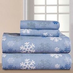 a stack of sheets with snowflakes on them next to a vase and window