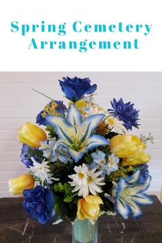 a vase filled with blue and yellow flowers on top of a table next to a sign that says spring cemetery arrangement