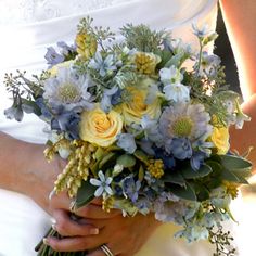 a bride holding a bouquet of yellow and blue flowers on her wedding day at the park