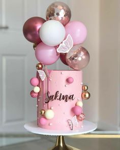 a pink cake with balloons on top and the word sakina written on it