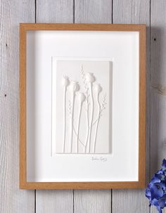 three white flowers in a wooden frame on a table next to blue flowers and a plant